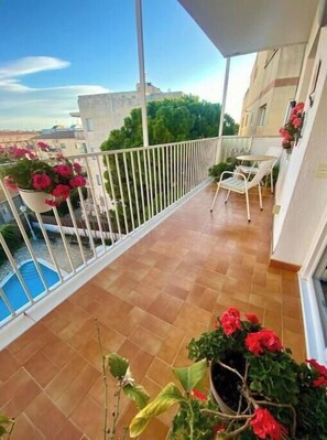Ein Balkon mit Fliesenboden, weißem Geländer, Blumentöpfen und Blick auf Gebäude und Bäume.