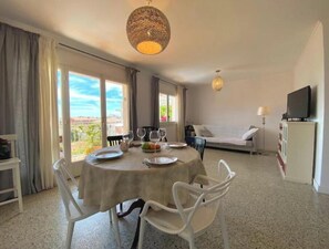 Ein Essbereich mit Tisch für zwei Personen, einer Couch, einem Fernseher und einem Balkon mit Blick.
