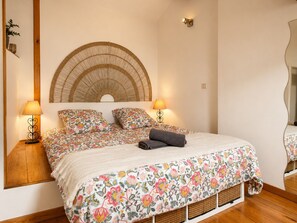 Ein Schlafzimmer mit einem Bett, zwei Nachttischlampen, einem gewobenen Kopfteil und einem Spiegel.