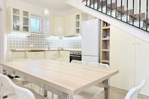 A modern kitchen with a wooden table, white chairs, and a staircase. - M463 – Marcelli, one-bedroom apartment with courtyard (Numana)