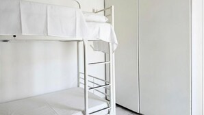 Un lit superposé avec un matelas blanc et une couverture blanche, une armoire blanche et un mur blanc.
