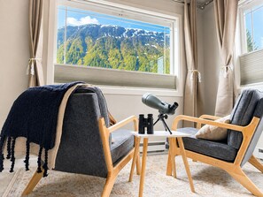 Ein Zimmer mit zwei Stühlen, einem Teleskop und einem Fenster mit Blick auf die Berge.