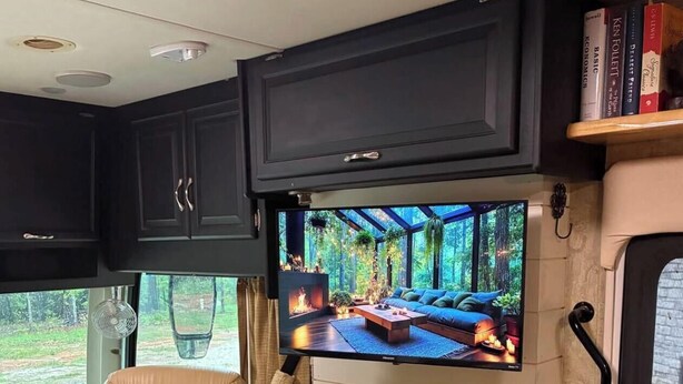 Una sala de estar acogedora con un sillón de cuero, chimenea y televisor de pantalla plana mostrando una escena de bosque.