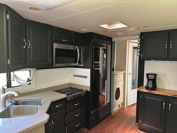 A compact kitchen with a stove, microwave, refrigerator, and coffee maker.