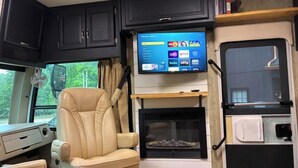 Un interior de autocaravana acogedor, con una zona de estar confortable, un televisor con servicios de streaming y una chimenea.