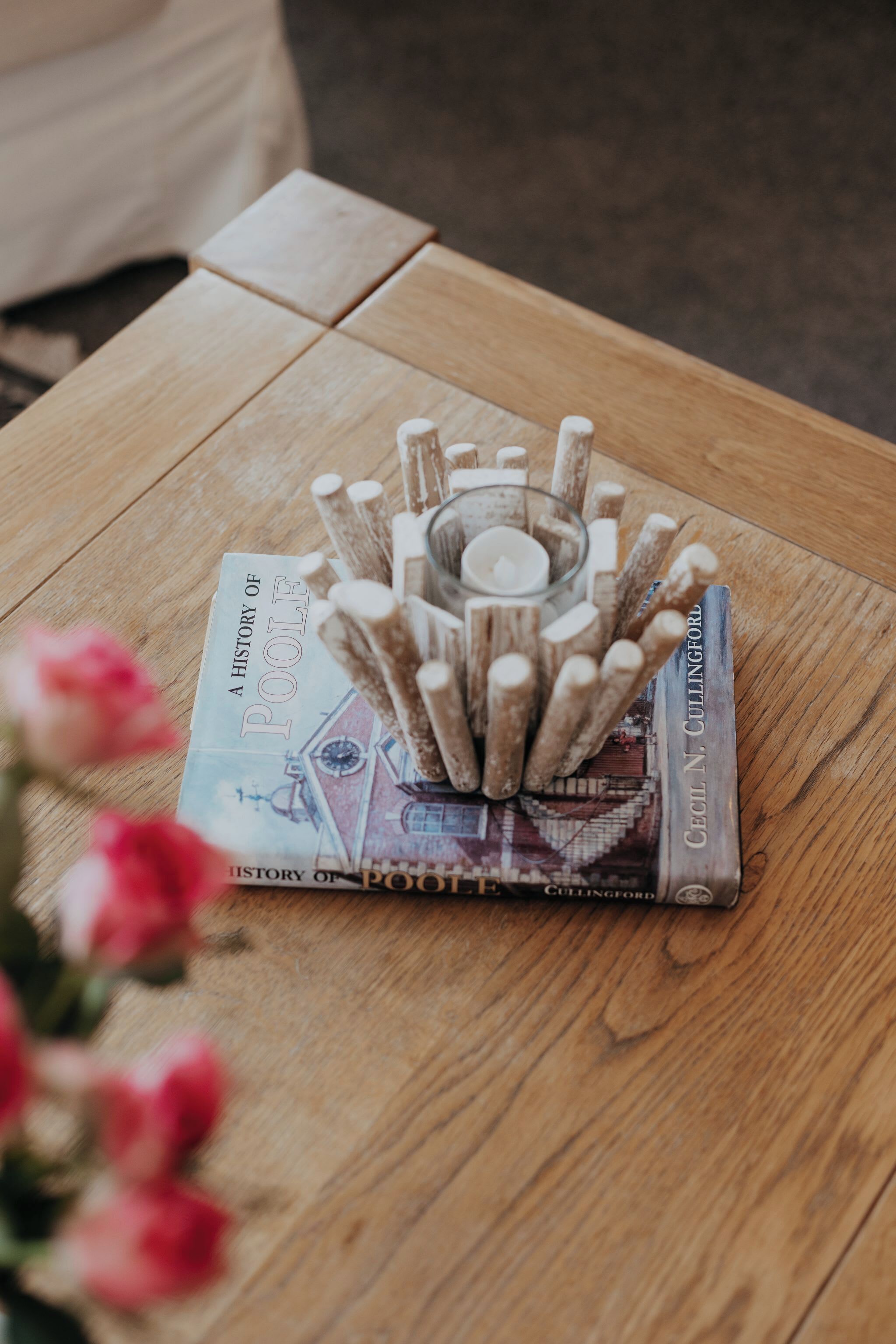 A wooden table with a book titled 'A History of Poole' and a candle holder with sticks.