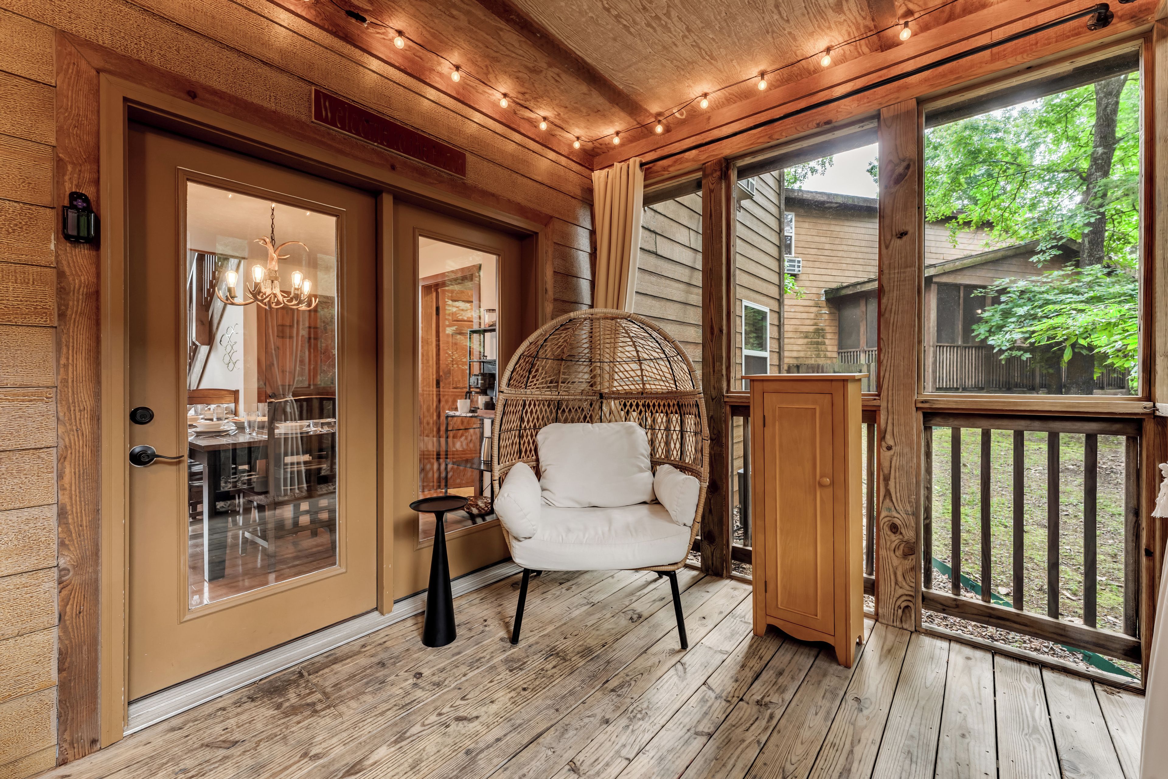 A wooden porch with a wicker chair, a dining table with chairs, and a view of the outdoors.