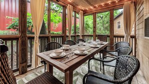 Un área de comedor al aire libre techada con una mesa de madera preparada para dos personas, rodeada de sillas de mimbre.
