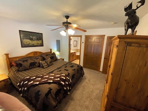 Quarto com cama, ventoinha no teto, guarda-roupa de madeira e uma porta.