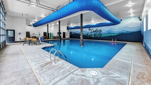 Una piscina con una estructura azul en techo, un mural con texto y una zona de estar con mesas y sillas.