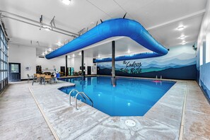 Piscina com estrutura azul sobreposta, mural com texto e área de estar com mesas e cadeiras.