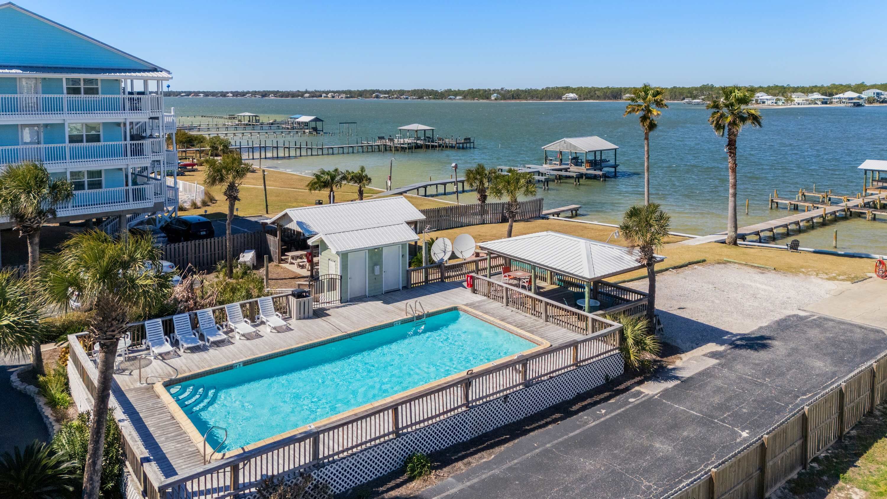 A pool area with a wooden deck, lounge chairs, and a view of the water.
