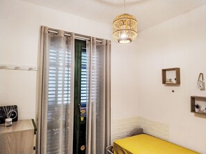 A room with a bed, a curtain, a hanging light fixture, and a wall-mounted shelf with items.