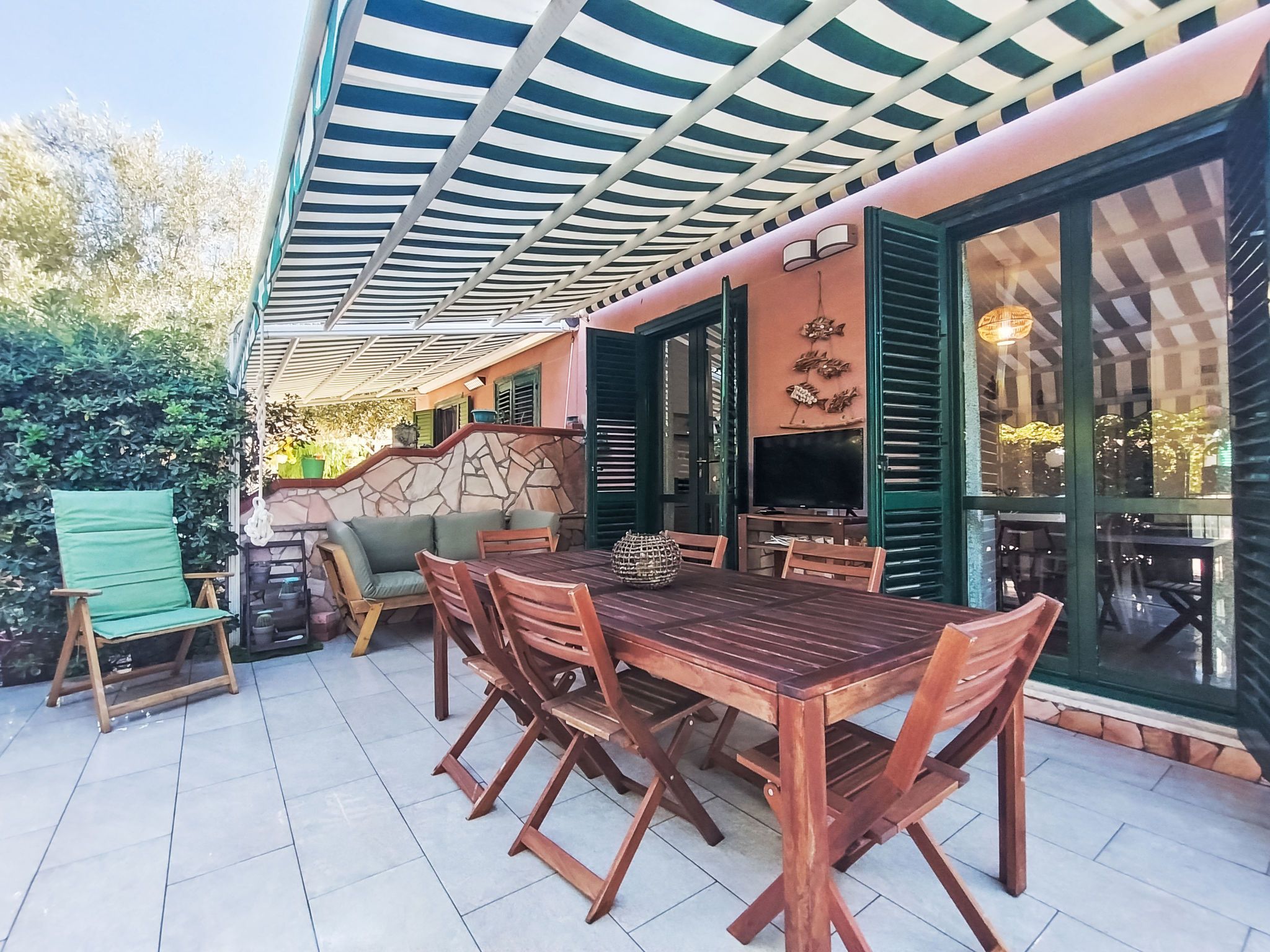Un patio al aire libre con mesa y sillas de madera, un área de estar cubierta y una pared de piedra.