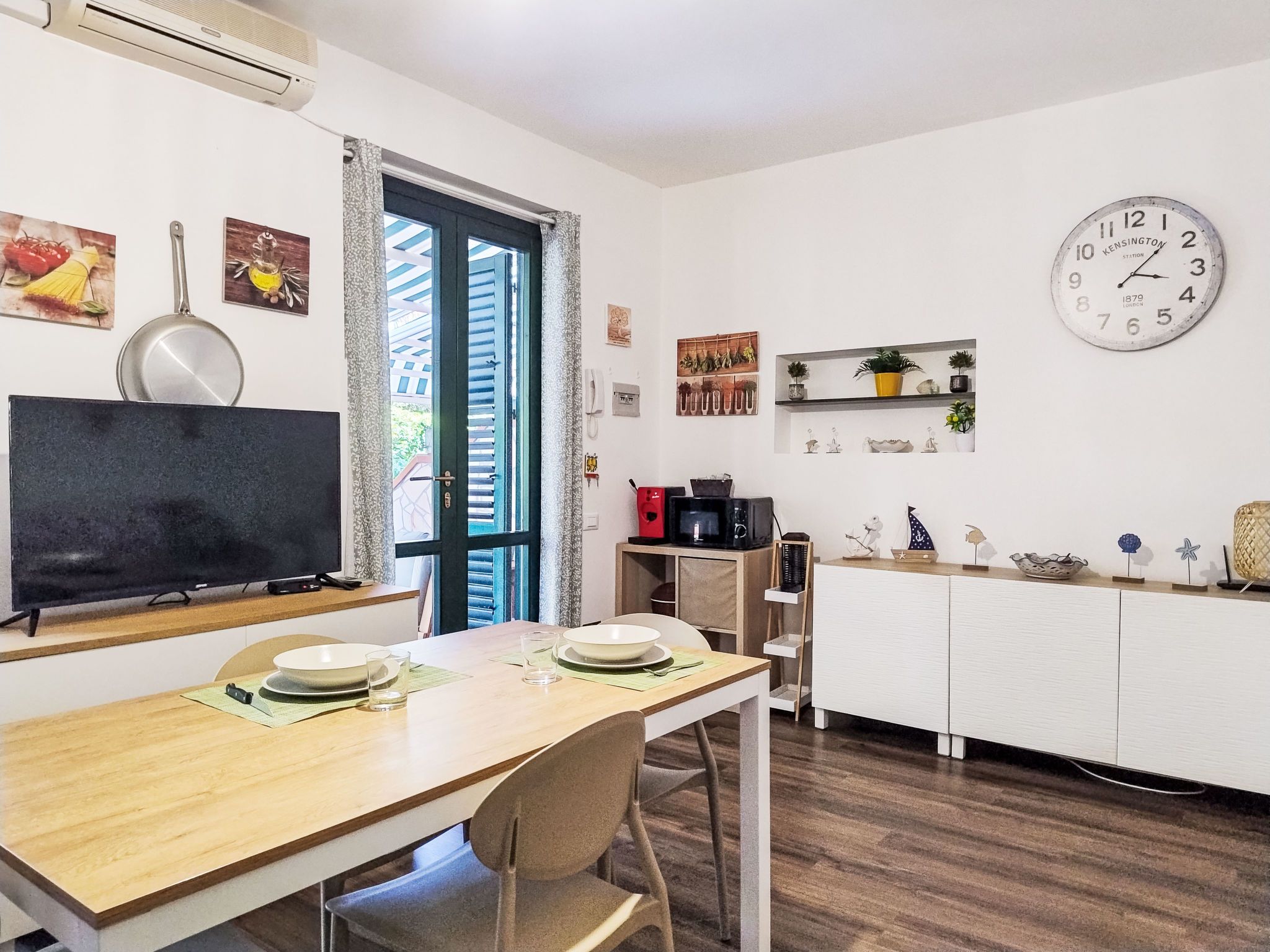 Una cucina moderna con zona pranzo, televisione a schermo piatto, forno a microonde e orologio a parete.