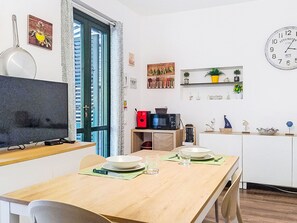 Ein Essbereich mit Holztisch, Stühlen, einem Fernseher und Küchengeräten.