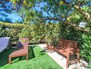 Un jardín con un banco de madera, una mesa pequeña y una planta en maceta.