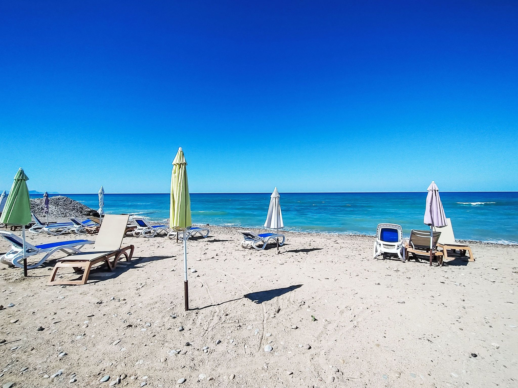 Une plage avec des transats et des parasols, un ciel dégagé et une mer calme.