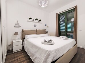 A neatly arranged bedroom with a bed, bedside tables, a lamp, and a window with blinds.