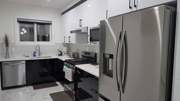 A modern kitchen with stainless steel appliances, a dishwasher, and a window above the sink. - The Blessed Family Home-2bed Rooms 2washrooms (Edmonton)