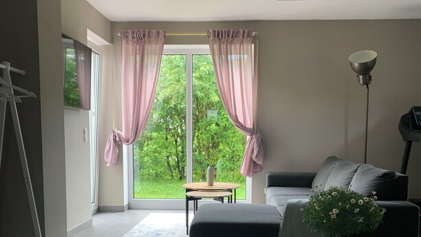 A modern living room with a sofa, a coffee table, a potted plant, and a view of greenery outside. - Top location! Apartment at the foot of the Rhön, forest on the doorstep. Pet friendly! (Dipperz)