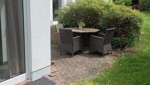 A patio with a table and chairs, surrounded by greenery and a white building. - Top location! Apartment at the foot of the Rhön, forest on the doorstep. Pet friendly! (Dipperz)