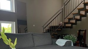 A modern living room with a grey sectional sofa, a wooden coffee table, a staircase with metal railings, and a window with a view of greenery. - Top location! Apartment at the foot of the Rhön, forest on the doorstep. Pet friendly! (Dipperz)
