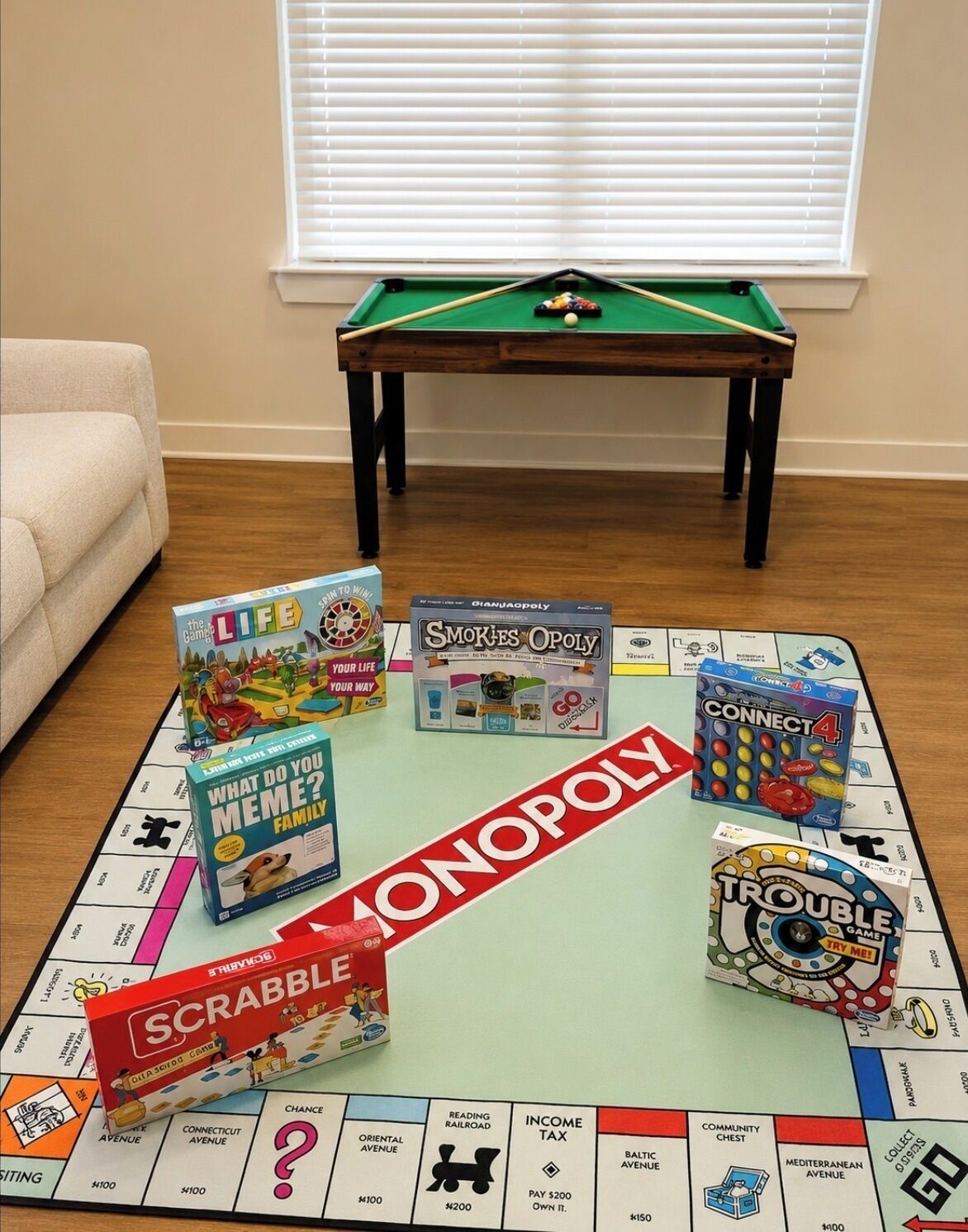 Un juego de mesa Monopoly junto a otros juegos de mesa y una mesa de billar en una habitación con pared color beige y una ventana.