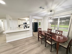 A modern kitchen with white cabinetry, a central island, and a dining area with wooden chairs and a table. - 3-bedroom 2-bath home in Beaumont (Beaumont)