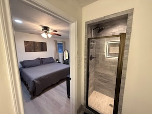 A bedroom with a bed, a ceiling fan, a window with curtains, and a shower area with a wooden door. - 3-bedroom 2-bath home in Beaumont (Beaumont)