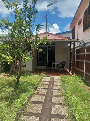 Ein Wohnhaus mit einem gepflasterten Weg, der zu einer überdachten Terrasse mit Tisch und Stühlen führt.