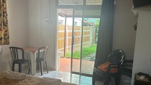 Una habitación con cama, una mesa con sillas, televisor y vista a un espacio exterior por una puerta corrediza.
