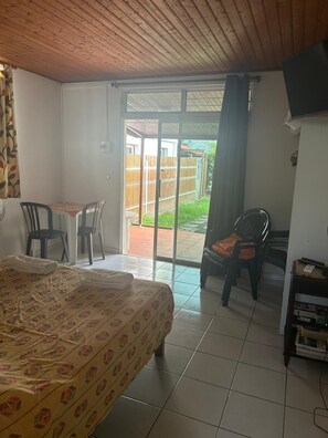 Ein Zimmer mit einem Bett, einem Tisch mit Stühlen, einem Fernseher und Blick durch eine Schiebetür auf einen Außenbereich.