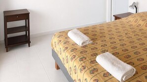 Un dormitorio con cama, televisor montado en la pared, mesita de noche y una puerta.