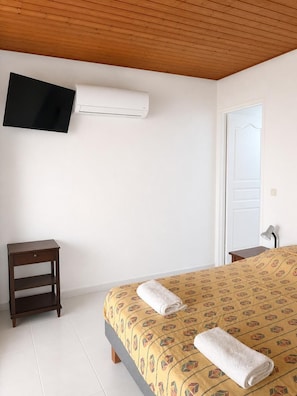 Ein Schlafzimmer mit Bett, Wandfernseher, Nachttisch und Tür.