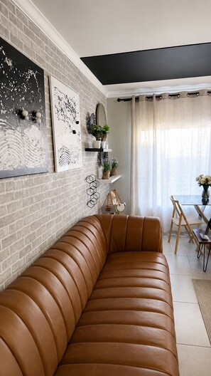 Ein modernes Wohnzimmer mit Ledersofa, Backsteinwand und Essbereich mit Tisch und Stühlen.