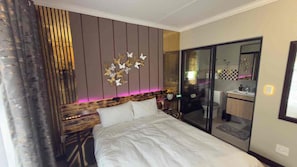 Quarto com cama, um objeto decorativo na parede e porta de vidro deslizante que dá para um banheiro.