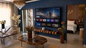 Ein modernes Wohnzimmer mit einem großen Flachbildfernseher, einem Holztisch und einer Sitzecke mit Glastisch und Stühlen.