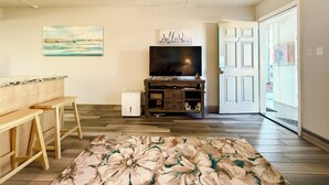 A living room with a TV, wooden furniture, a patterned rug, and a door leading outside. - Steps from the Beach with Gulf View Ground Floor (Fort Walton Beach)
