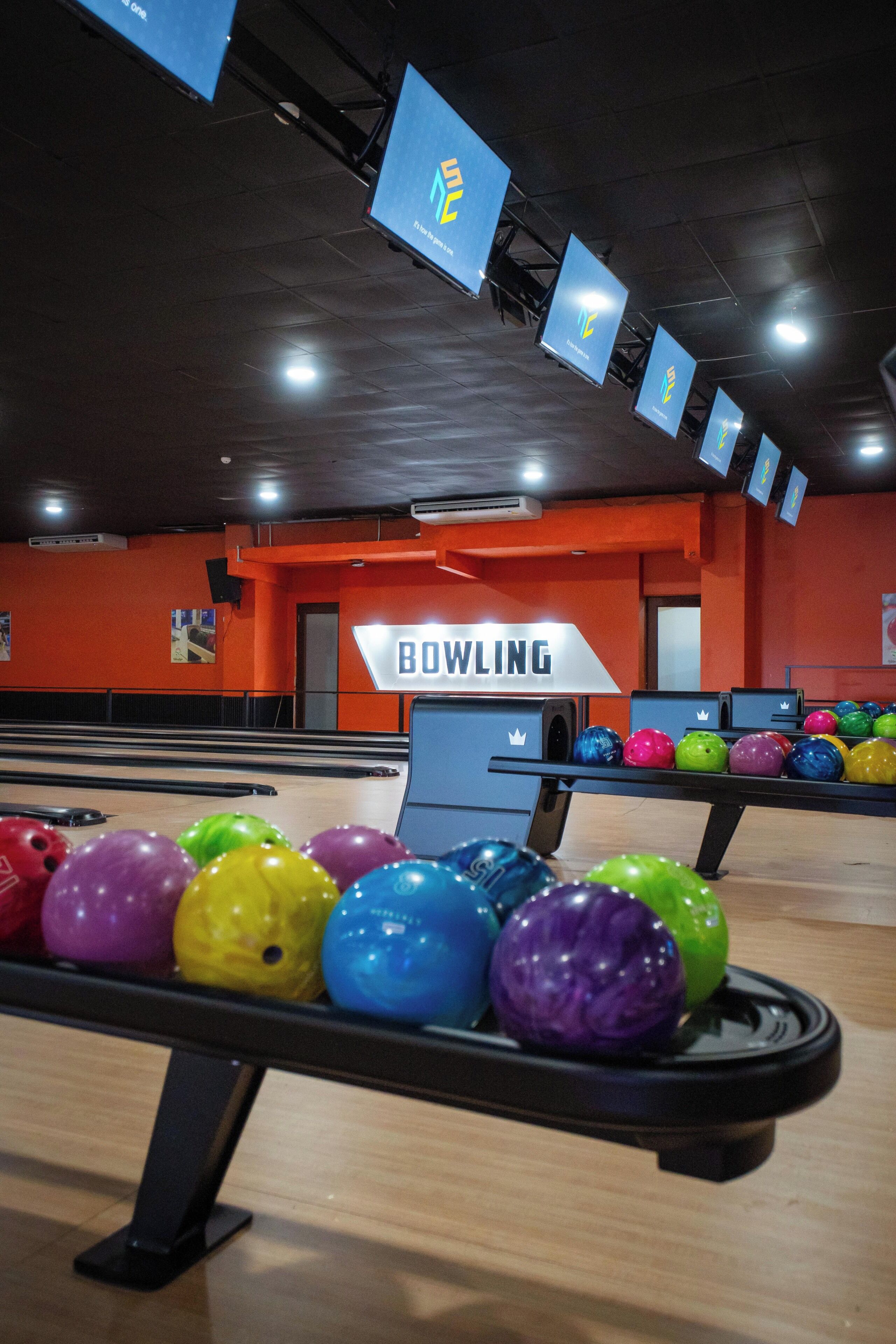 A bowling alley with multiple lanes, colorful bowling balls, and overhead signs.