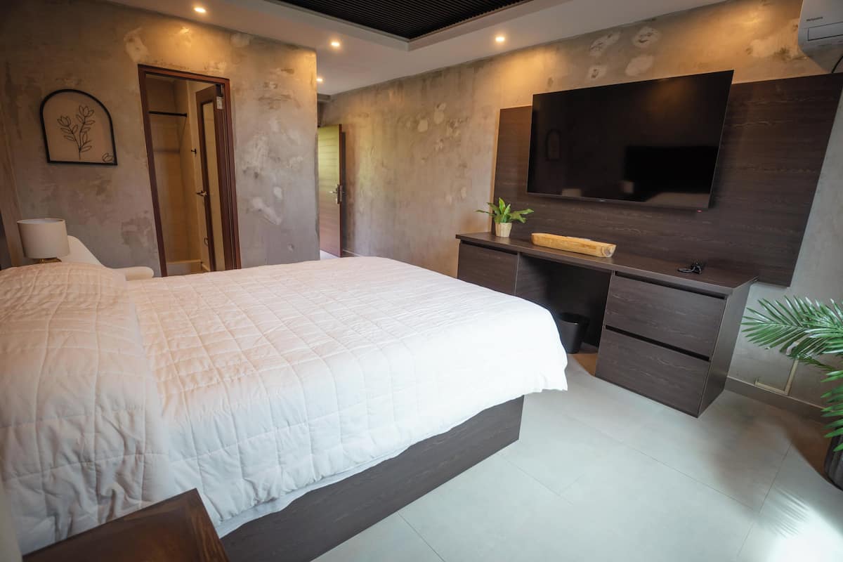 Un dormitorio moderno con una cama grande, un escritorio empotrado, un televisor y un espejo.
