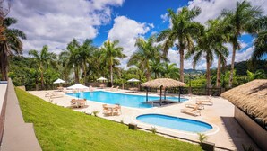 Un área de piscina con sillas de descanso, sombrillas y palmeras.