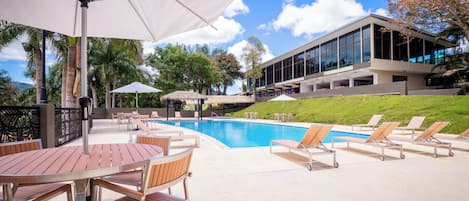 A poolside area with lounge chairs, umbrellas, and a modern building in the background.
