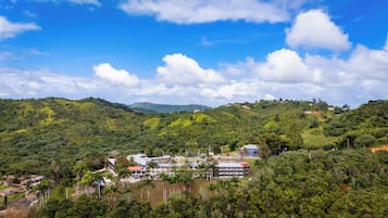 Un paisaje montañoso con un pequeño conjunto de edificios que incluye varias construcciones, rodeado de vegetación exuberante y un cielo despejado.