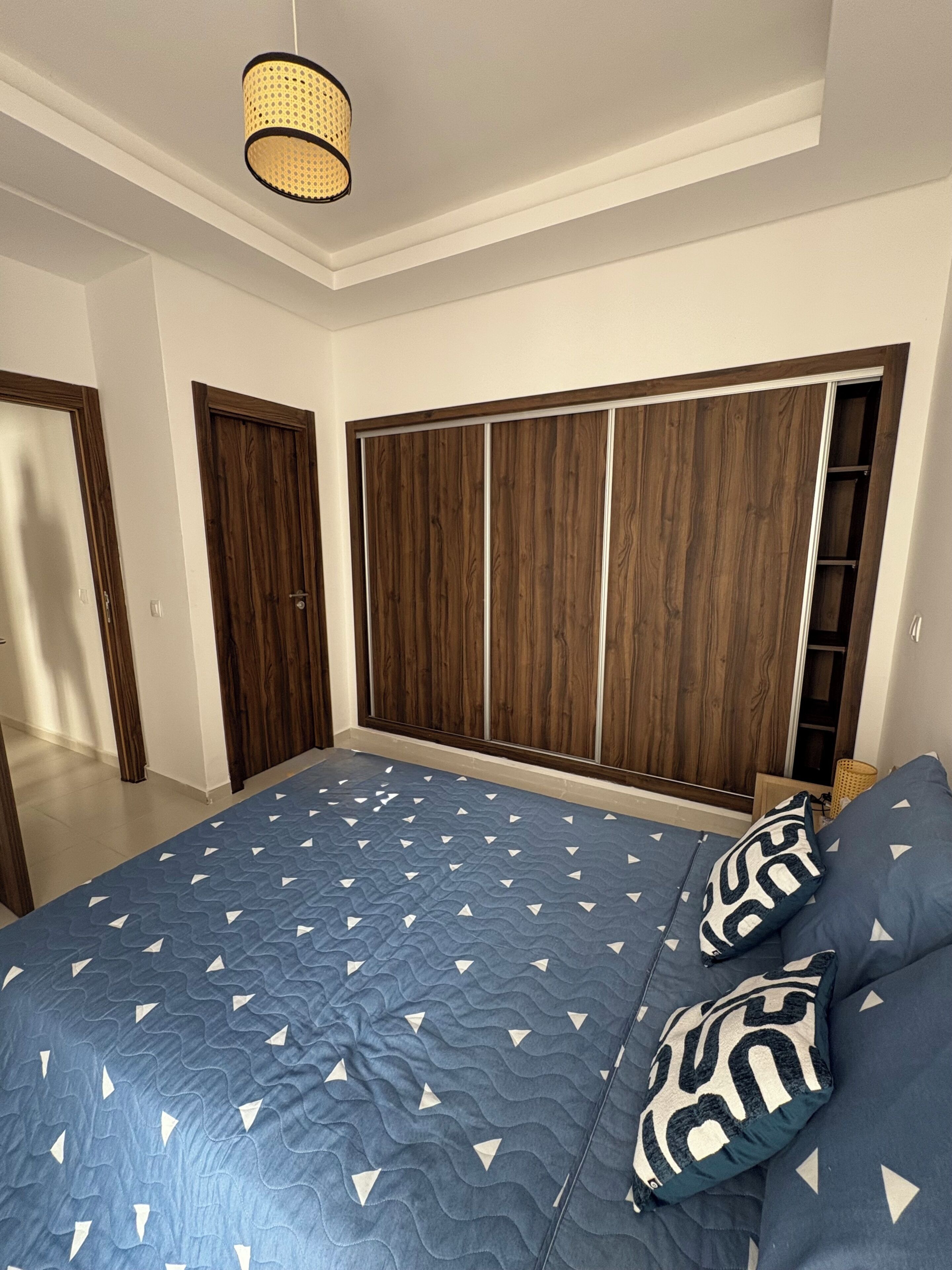 A bedroom with a large bed, wooden wardrobe, and a hanging light fixture.