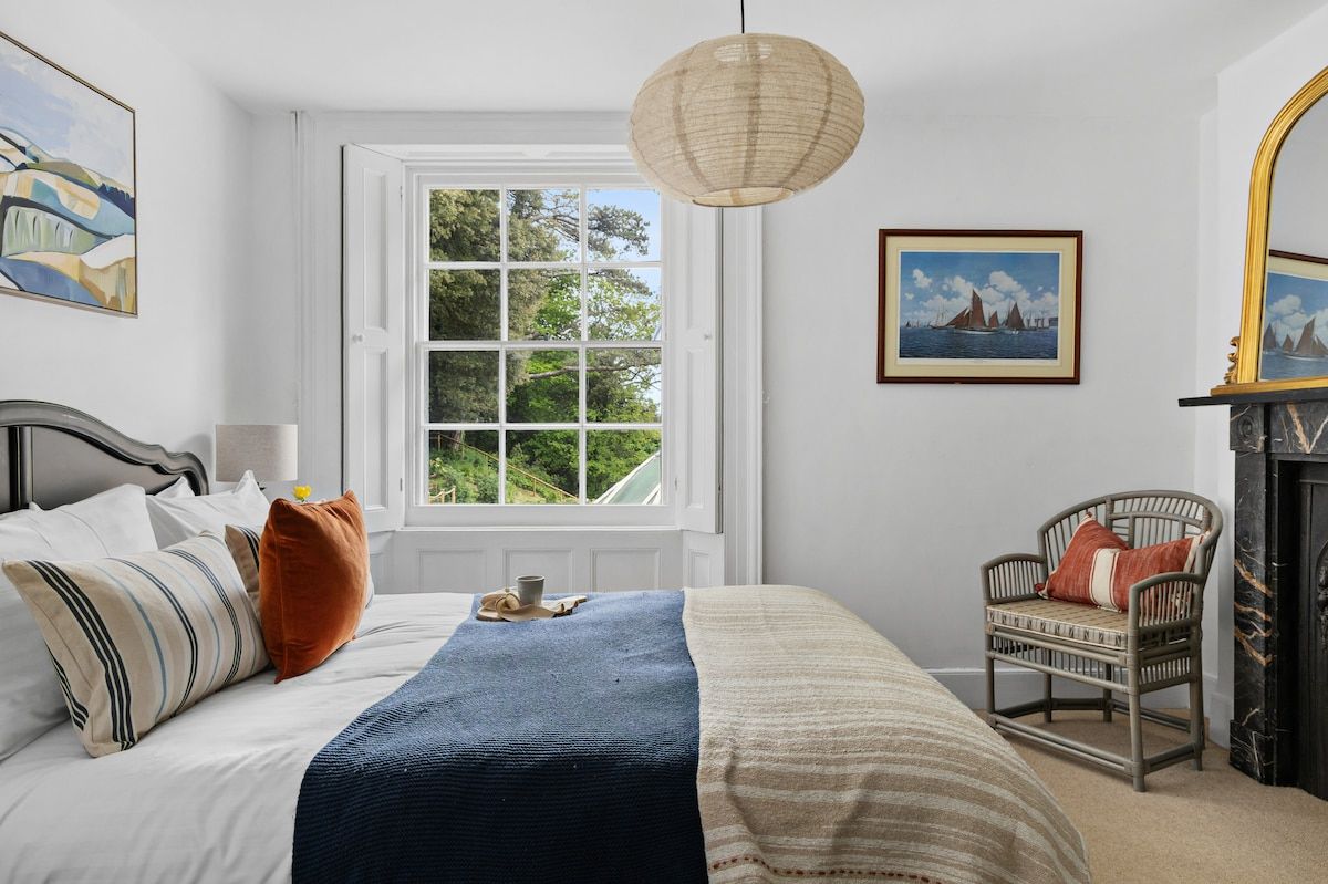A bedroom with a bed, a window, a chair, and a fireplace.