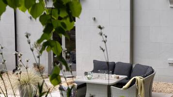 An outdoor seating area with a wicker sofa, a glass-top table, and a potted plant.