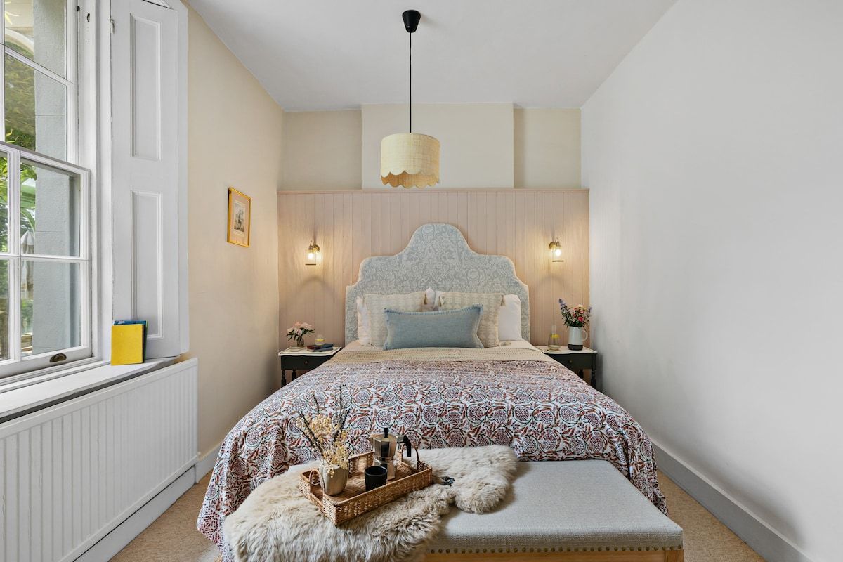 A bedroom with a large bed, a window, a bedside table, and a hanging light fixture.