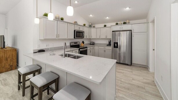 A modern kitchen with white cabinets, stainless steel appliances, and a central island with stools. - Walk to Brownwood! Spacious 3BR | Golfcart + BBQ (The Villages)