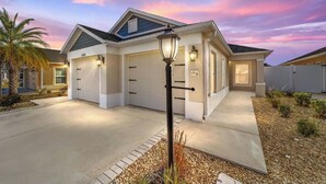 A modern two-story house with a garage, a well-lit entrance, and a landscaped front yard. - Walk to Brownwood! Spacious 3BR | Golfcart + BBQ (The Villages)